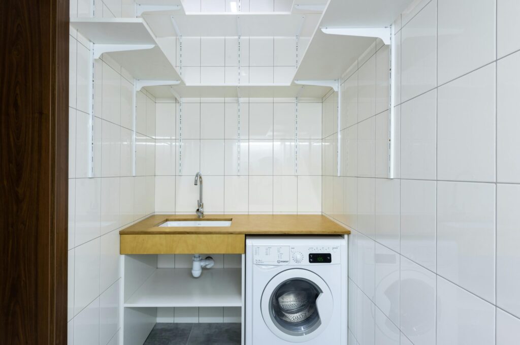 Modern laundry area with white tiled walls, washing machine, and built-in shelves.