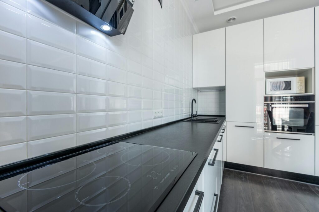 Interior of modern light white kitchen furnished with white cupboards and appliances with wooden floor and tiled wall