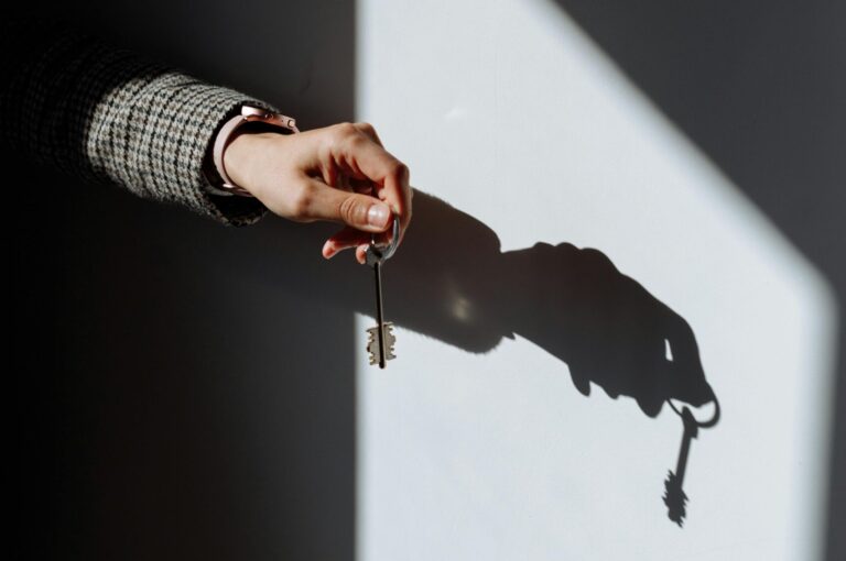 Hand with a key casting a dramatic shadow on a wall, symbolizing property or ownership.