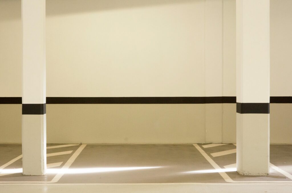 A minimalist view of a well-lit, empty parking garage interior featuring structural posts.